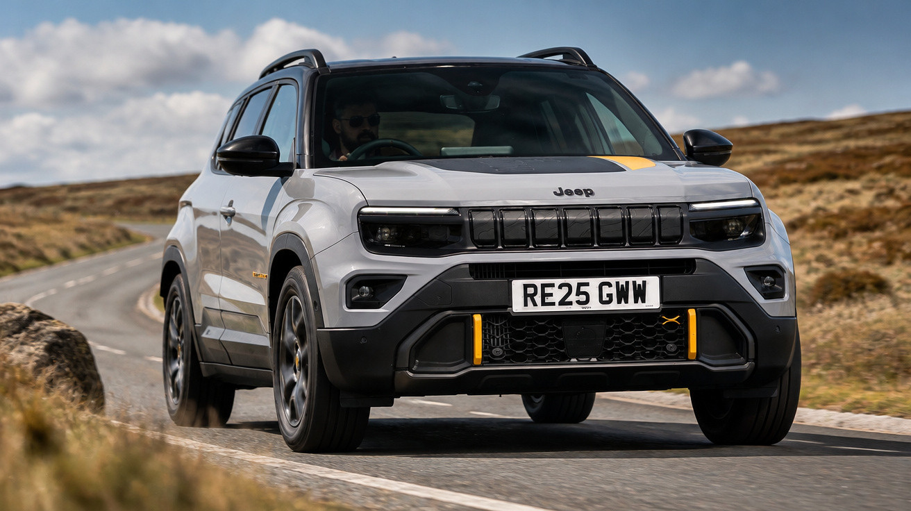 Jeep SUV gris roulant sur route de campagne avec ciel bleu et nuages blancs en arrière-plan.