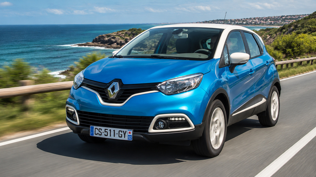 Voiture Renault bleue roulant sur une route côtière avec vue sur la mer et paysage verdoyant.